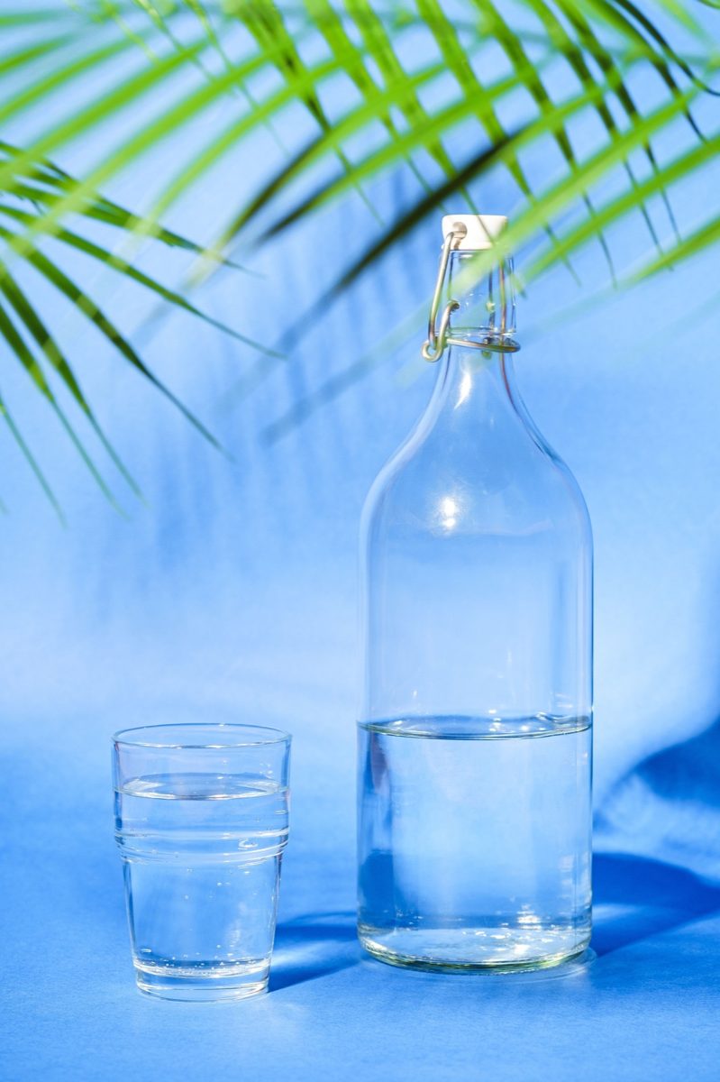水色の背景に置かれた水の瓶とグラス